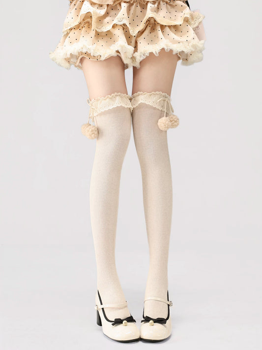 White tights with lace details and pom-poms worn by a person on a light gray background