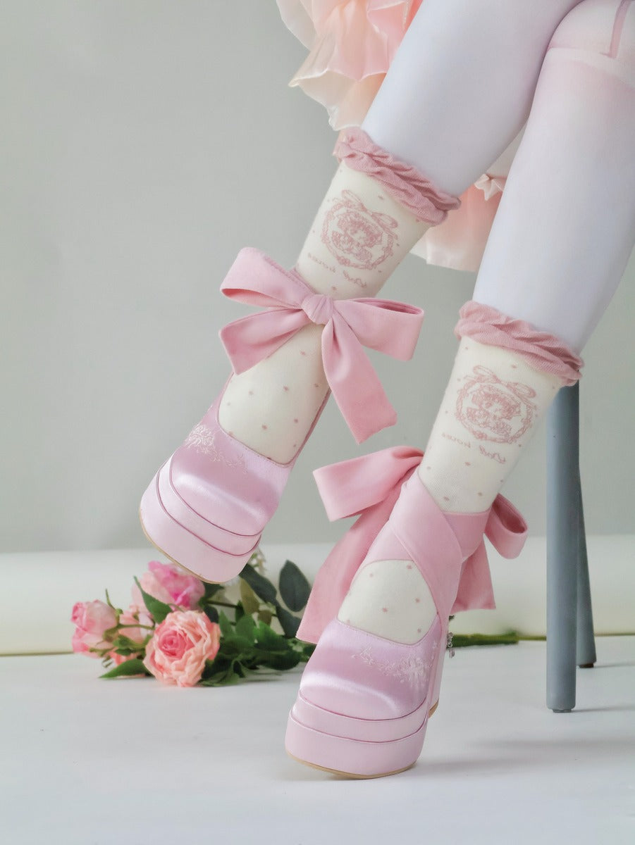 Pink and white striped socks with bows worn by a person, sitting on a chair with flowers in the background.