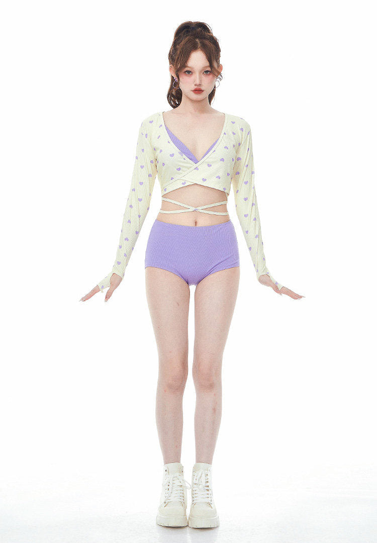 Woman wearing a light-colored long-sleeve top with a criss-cross design and purple high-waisted shorts on a white background.