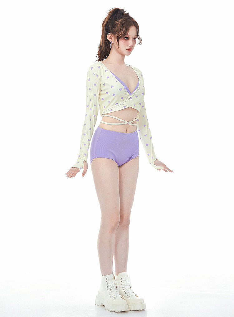 Woman wearing a light-colored long-sleeve top and purple high-waisted swimsuit on a white background