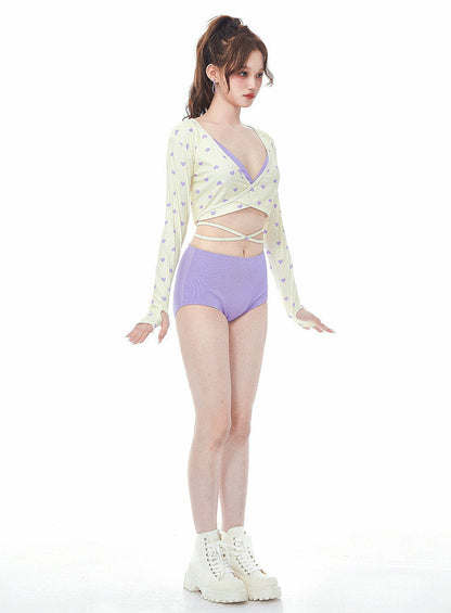 Woman wearing a light-colored long-sleeve top and purple high-waisted swimsuit on a white background