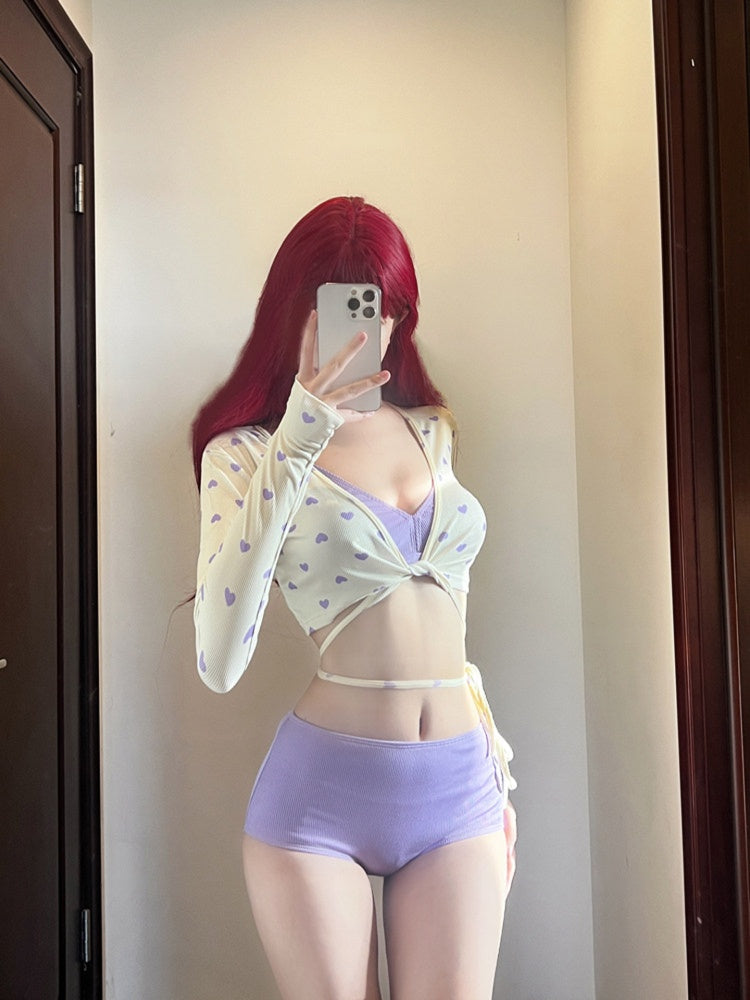 Person wearing a light-colored sheer top and purple bikini swimsuit in front of a mirror.