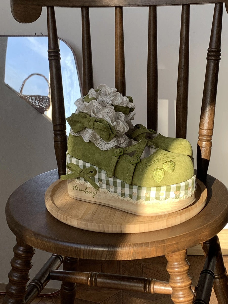 Green decorative shoes on a wooden chair with a checkered box and floral arrangement.
