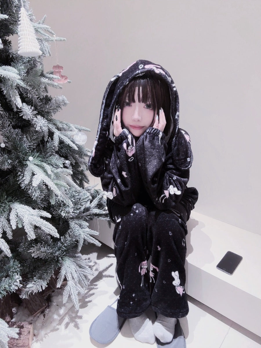 Person wearing a black hoodie with white patterns sitting next to a decorated Christmas tree.