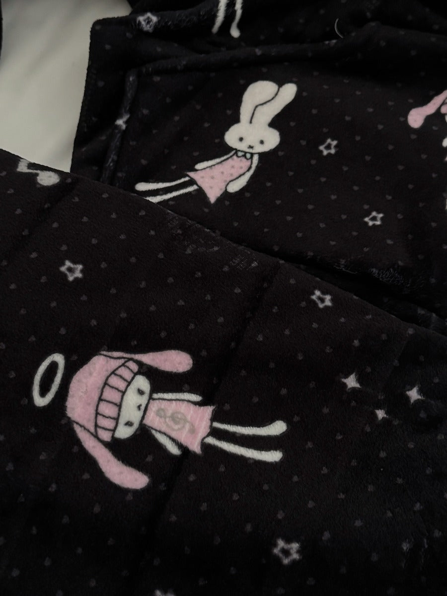 Black fleece pajama fabric with a white polka dot pattern, featuring cartoon bunny and angel character prints in pink and white.