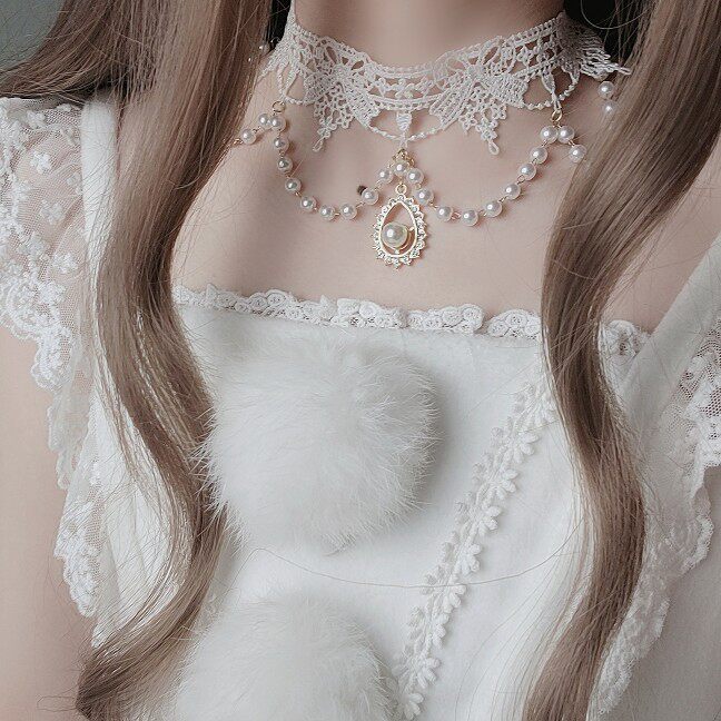Close-up of a person wearing a delicate pearl necklace and lace garment.
