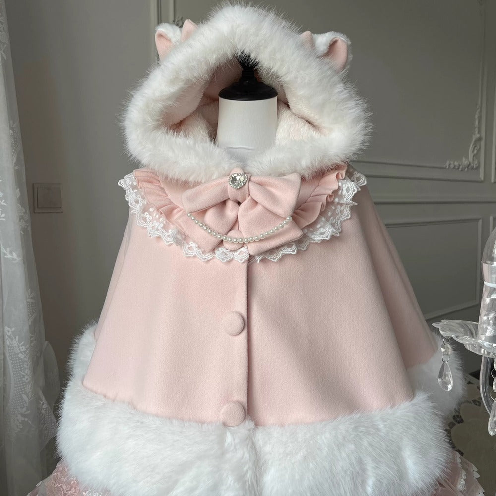 A light pink hooded cape with white faux fur trim, cat ears on the hood, a large bow at the neckline, and lace detailing, displayed on a mannequin torso indoors.