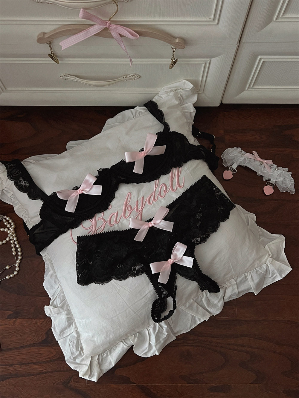 Black lace babydoll with pink bows on a white pillow, with a hanger in the background.