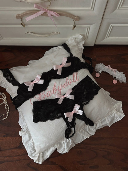 Black lace babydoll with pink bows on a white pillow, with a hanger in the background.