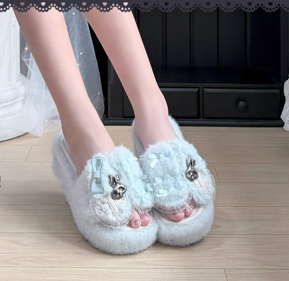 A person wearing fluffy light blue slip-on slippers with decorative bows, bunny embellishments, and clear embellishments, standing on a light wood floor.