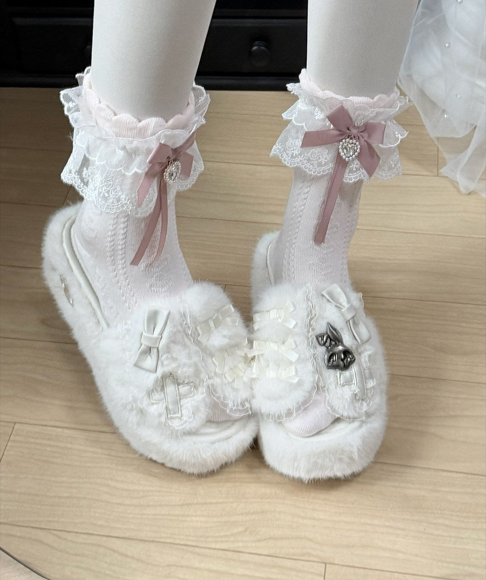 White fuzzy Mary Jane platform shoes with lace ruffles, pink ribbon bows, and decorative bows on the toes, shown on a mannequin's feet against a light wood floor.