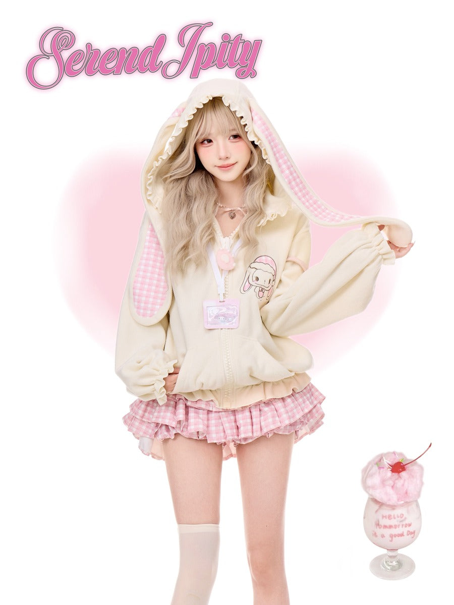 A young woman models a cute pastel cream hoodie with pink gingham bunny ears and a matching pink ruffled skirt. The 'Serendipity' is written in pink script at the top left, and a small dessert cup graphic is at the bottom right.