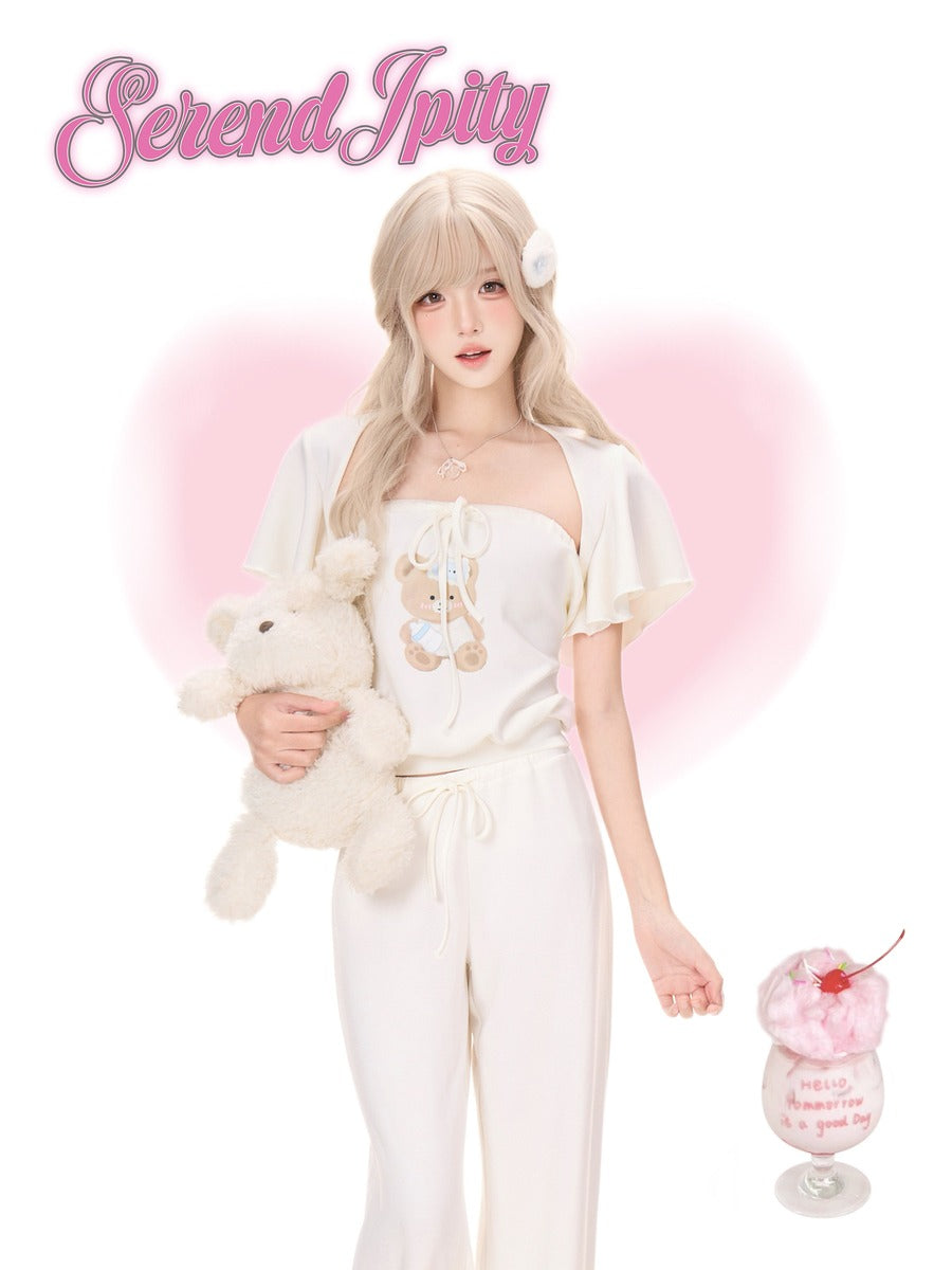 A young woman with long blonde hair stands against a white background with a pink heart-shaped glow, wearing a cream-colored two-piece outfit with a teddy bear graphic on the top. She is holding a cream teddy bear and a pink milk dessert in a glass.
