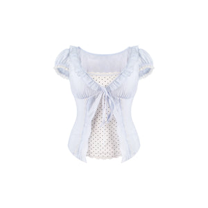 A light blue ruffled short-sleeve blouse with a tie at the neckline, layered over a white polka-dot top, shown against a plain white background.