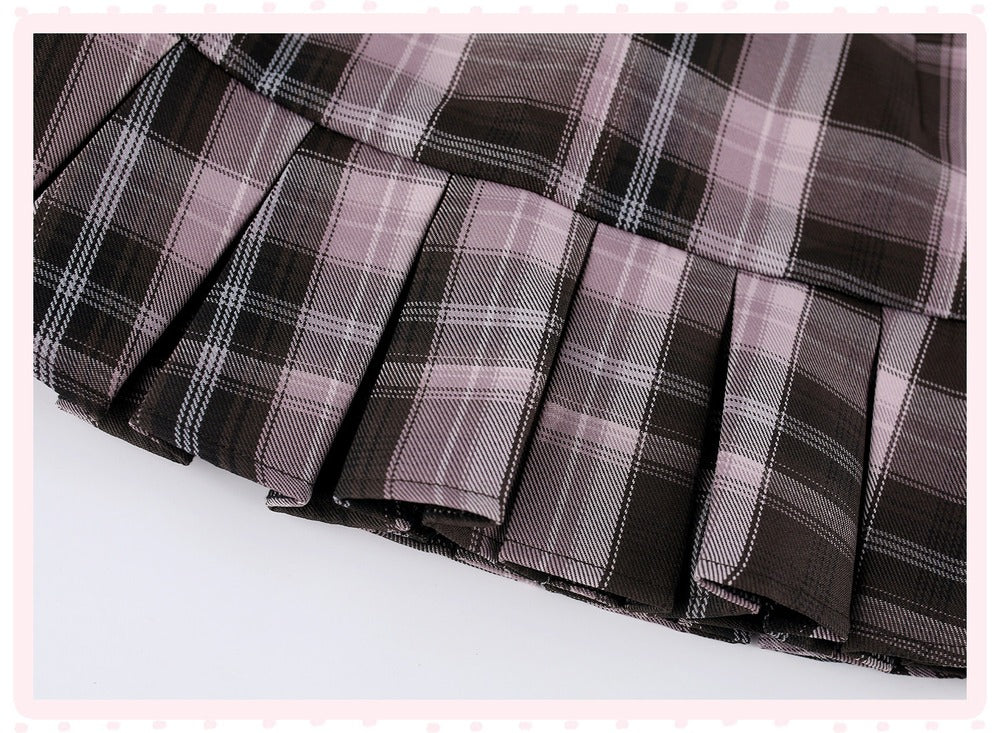 A close-up of a pleated plaid skirt in a dark brown, black, and dusty pink tartan pattern, shown against a white background with a light pink decorative border.