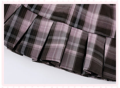 A close-up of a pleated plaid skirt in a dark brown, black, and dusty pink tartan pattern, shown against a white background with a light pink decorative border.