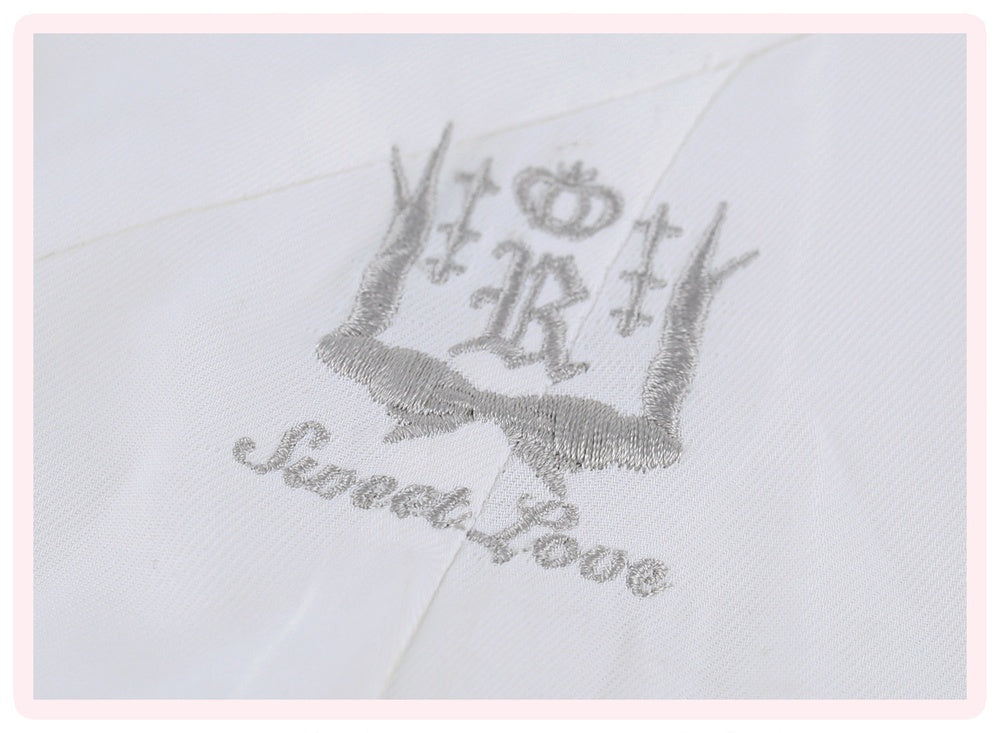 A close-up of a white embroidered monogram featuring a crown, antlers, and the words 'Sweet Rose' in silver thread.