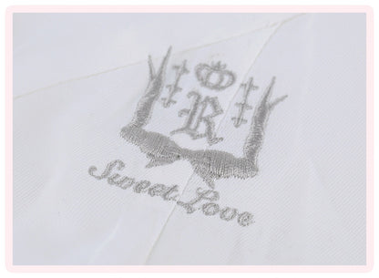 A close-up of a white embroidered monogram featuring a crown, antlers, and the words 'Sweet Rose' in silver thread.