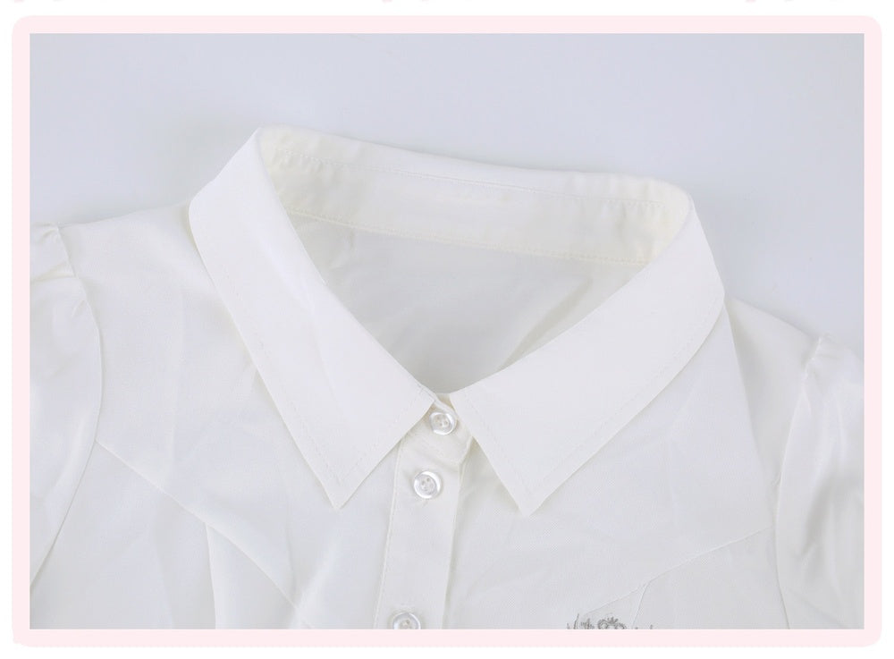 Close-up of a white long-sleeve collared blouse with a buttoned front and pointed collar, shown against a light gray background with a thin pink border.