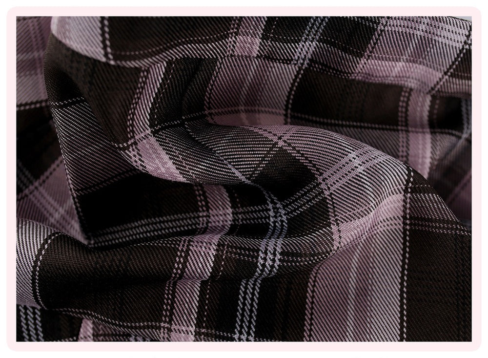 A close-up of draped plaid fabric with a black base and intersecting light pink and white stripes, framed by a thin pink border.