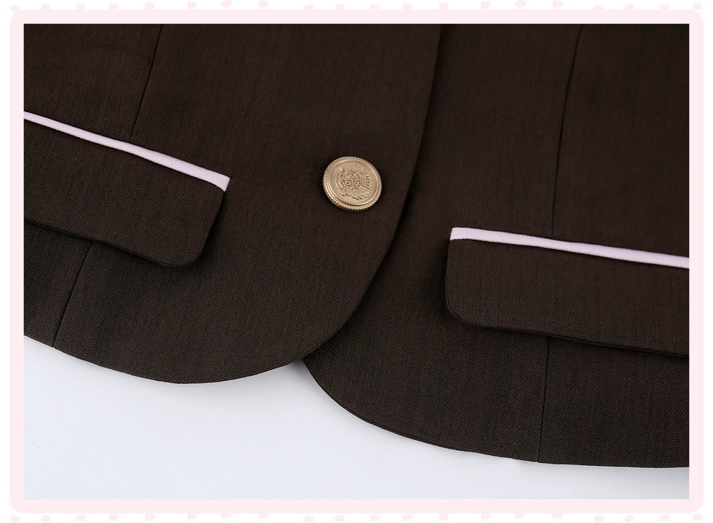 Close-up of a dark brown blazer featuring light pink piping along the pocket flaps and a single gold button.