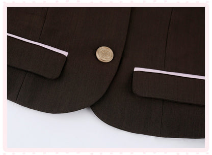 Close-up of a dark brown blazer featuring light pink piping along the pocket flaps and a single gold button.