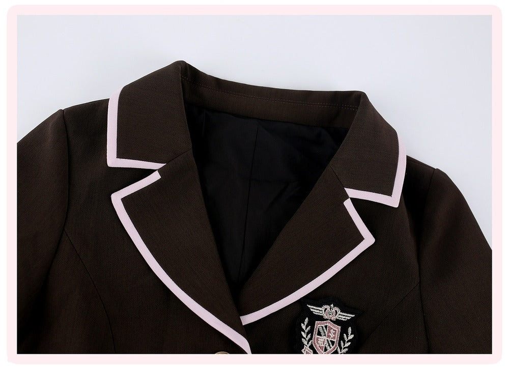 A close-up of a dark brown blazer featuring light pink piping along the lapels and a school crest patch on the left chest, set against a light gray background with a pink border.