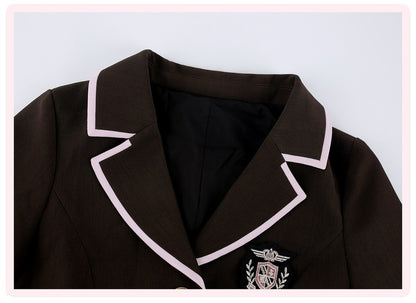A close-up of a dark brown blazer featuring light pink piping along the lapels and a school crest patch on the left chest, set against a light gray background with a pink border.