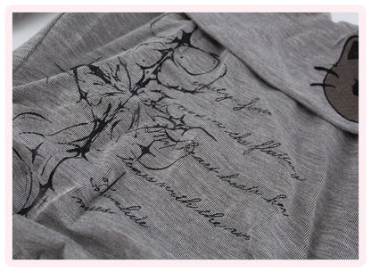 Close-up of a gray fabric garment with black floral line art, cursive script text, and a partial cartoon face patch on the sleeve.