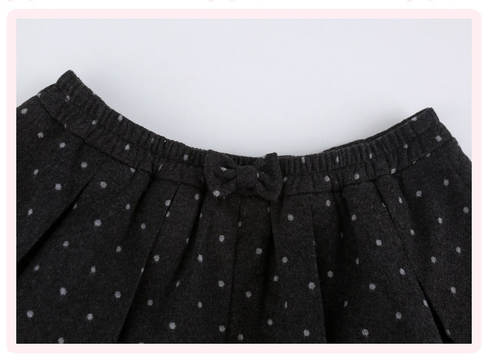 Close-up of a black pleated skirt with a white polka dot pattern and a matching fabric bow at the elastic waistband.