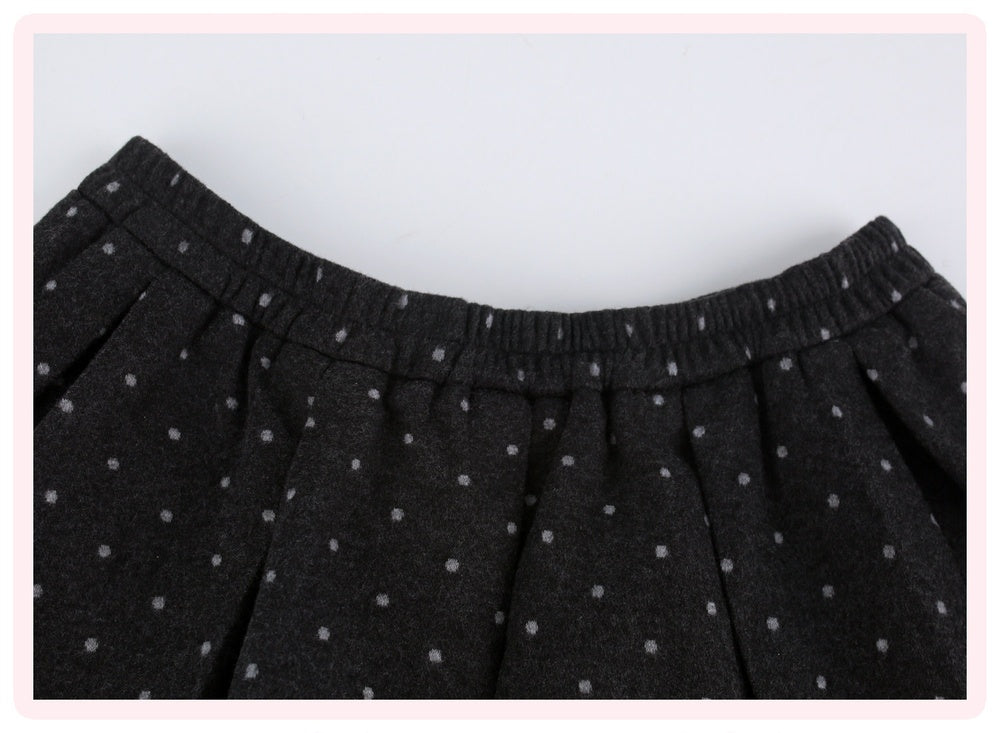 Close-up of a black pleated skirt with a small white polka dot pattern and an elastic waistband, framed by a light pink border.