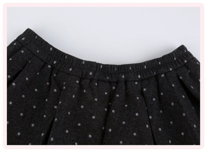 Close-up of a black pleated skirt with a small white polka dot pattern and an elastic waistband, framed by a light pink border.