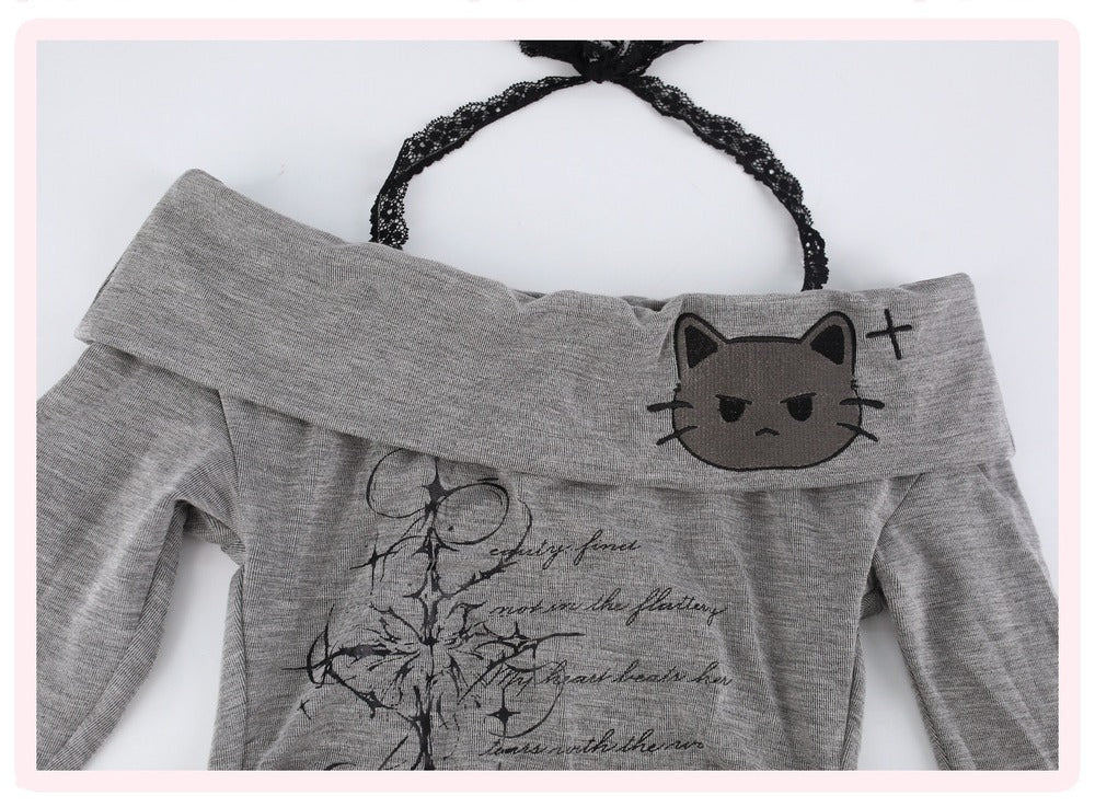 A gray off-the-shoulder long-sleeve top featuring a cartoon cat face patch on the shoulder and a black graphic print on the front, displayed on a white background with a black lace loop.