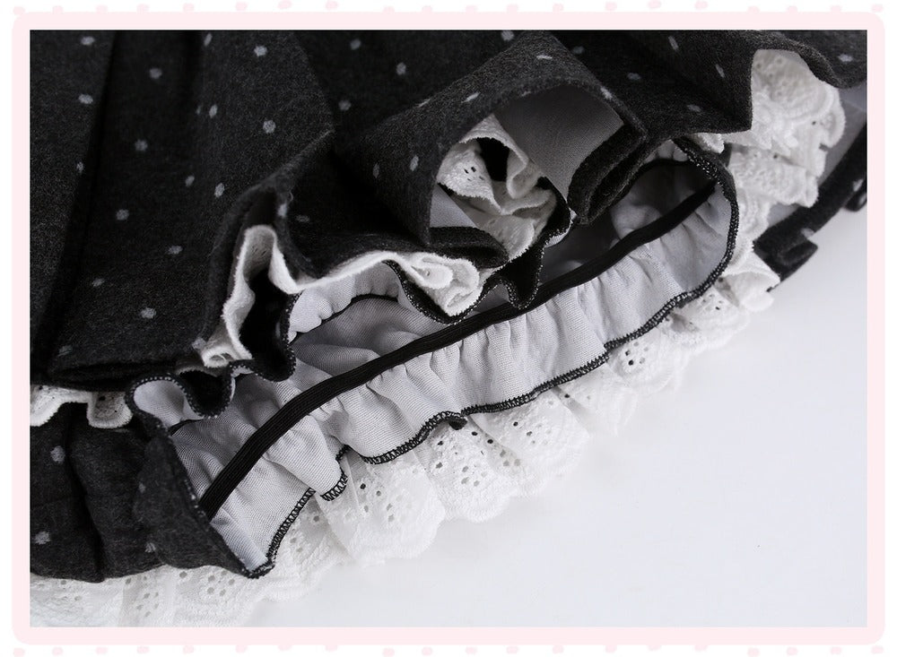Close-up of a black fabric skirt with small white polka dots, layered ruffles, and white eyelet lace trim on a white background.