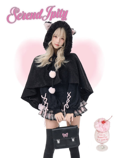 A model wearing a black furry hooded cape with pink pom-poms and a matching black lace-up skirt, holding a black handbag with a pink bow. The image has a pink heart-shaped glow, a pink 'Serendipity' logo at the top left, and a pink dessert cup at the bottom right.