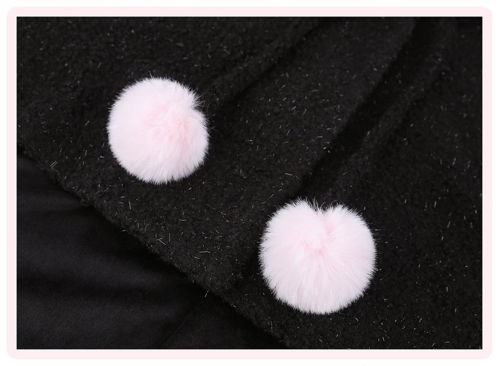 Close-up of a black textured garment featuring two fluffy light pink pom-pom buttons or decorative accents.