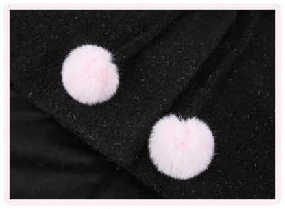 Close-up of a black textured garment featuring two fluffy light pink pom-pom buttons or decorative accents.