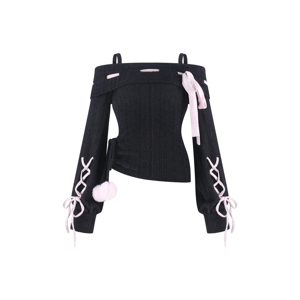 A black ribbed off-the-shoulder long-sleeve top with light pink accents, including side laces, a bow, and a pom-pom detail, shown against a plain white background.