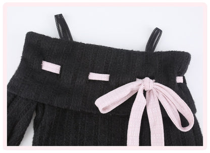 Close-up of a black ribbed knit garment with thin shoulder straps, small light pink rectangular accents, and a large light pink bow at the front, shown on a white background with a pink border.