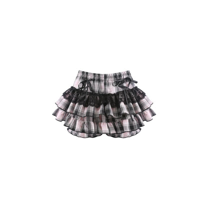 A tiered ruffle skirt in a black, white, and pink plaid pattern with sheer black mesh layers and matching black ribbon ties at the waist, shown against a plain white background.