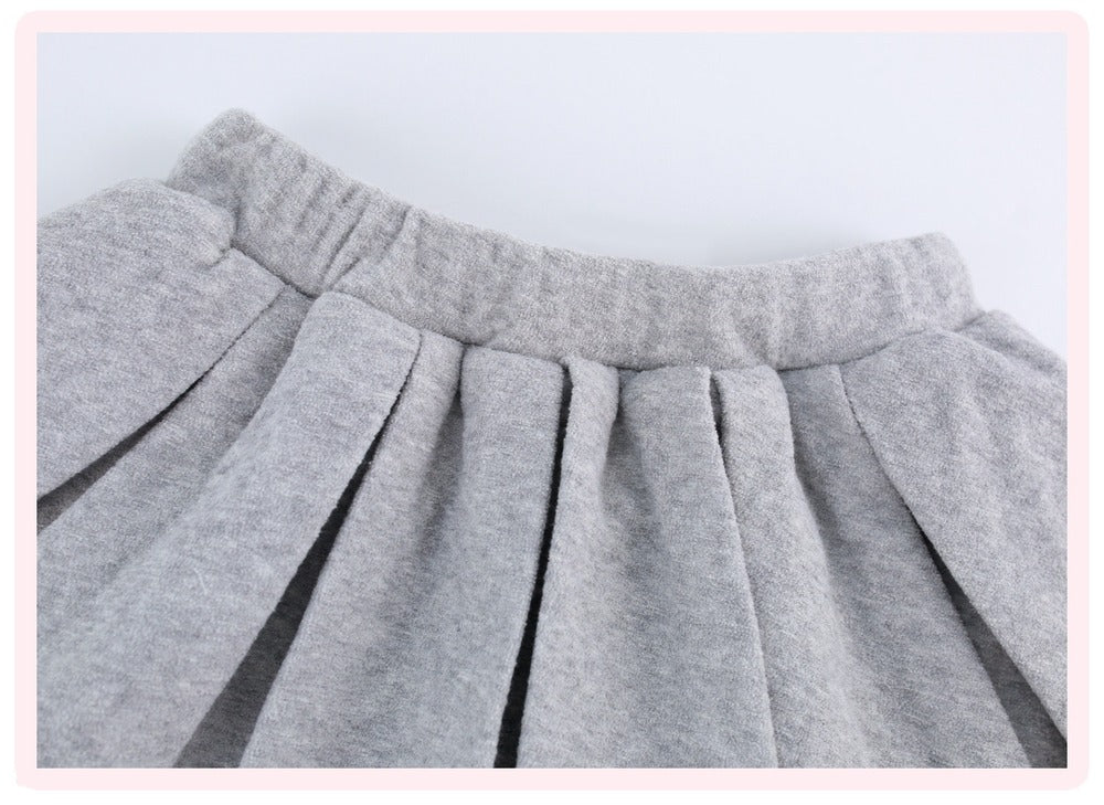 Close-up of a light gray pleated fabric garment, showing the waistband and gathered pleats against a plain light background.