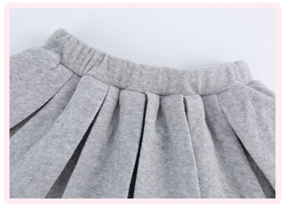 Close-up of a light gray pleated fabric garment, showing the waistband and gathered pleats against a plain light background.