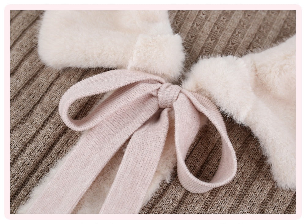 Close-up of a soft pink ribbon bow tied around a cream faux-fur collar on a ribbed taupe knit garment.