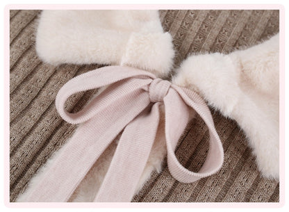 Close-up of a soft pink ribbon bow tied around a cream faux-fur collar on a ribbed taupe knit garment.