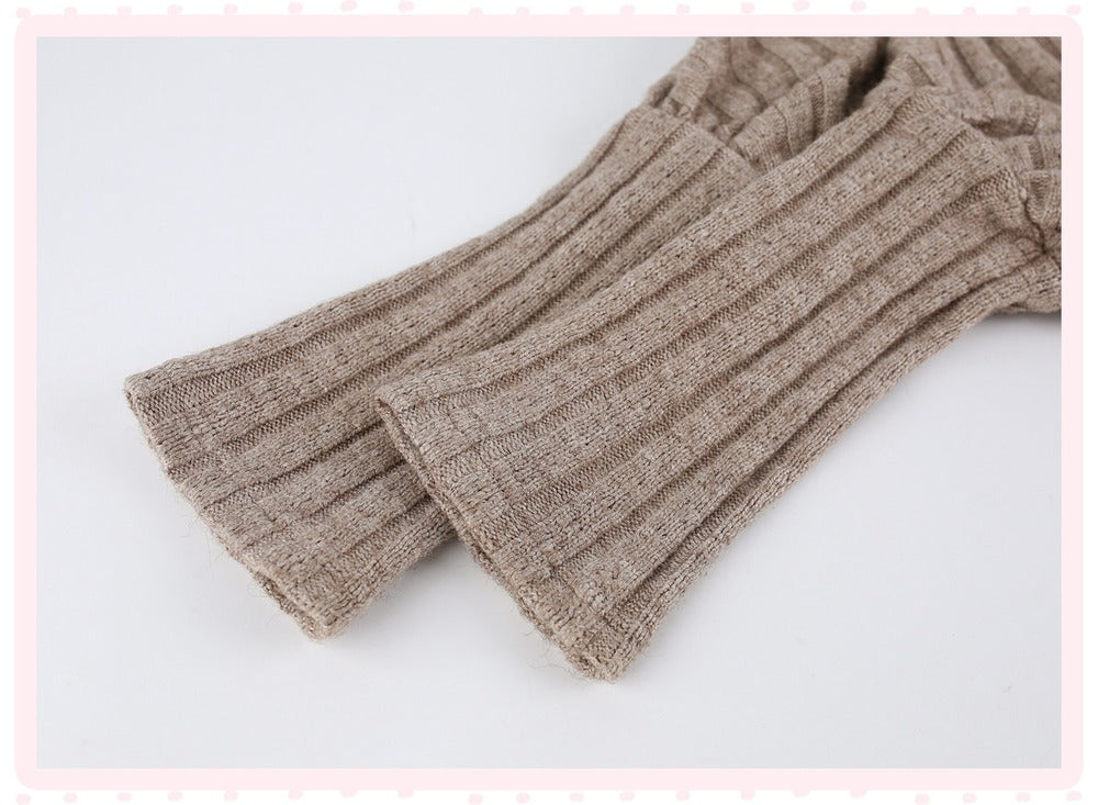 Close-up of a ribbed knit garment in a warm taupe-beige color, showing the texture and folds of the fabric against a light background.