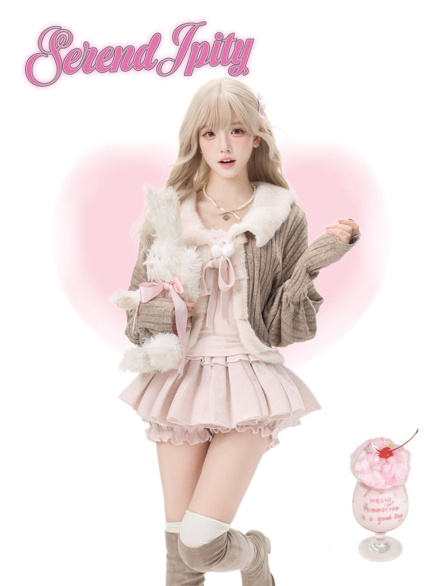 A young woman models a pastel pink and beige Lolita-style outfit with a pleated skirt, cardigan, and white faux-fur collar details, holding a plush toy. The name 'Serendipity' is written in pink script at the top left, and a small pink cup graphic appears at the bottom right.