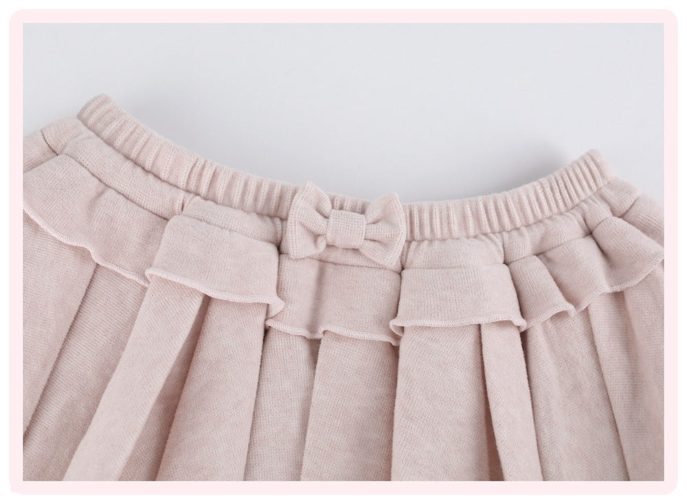 Close-up of a light pink pleated skirt with a matching bow detail at the elastic waistband.