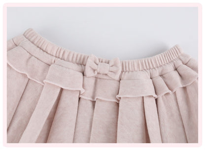 Close-up of a light pink pleated skirt with a matching bow detail at the elastic waistband.