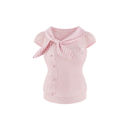 A pink short sleeve top with a pink and white gingham bow collar, ruffled cap sleeves, a button-up front, and a small heart applique on the chest, shown on a plain white background.