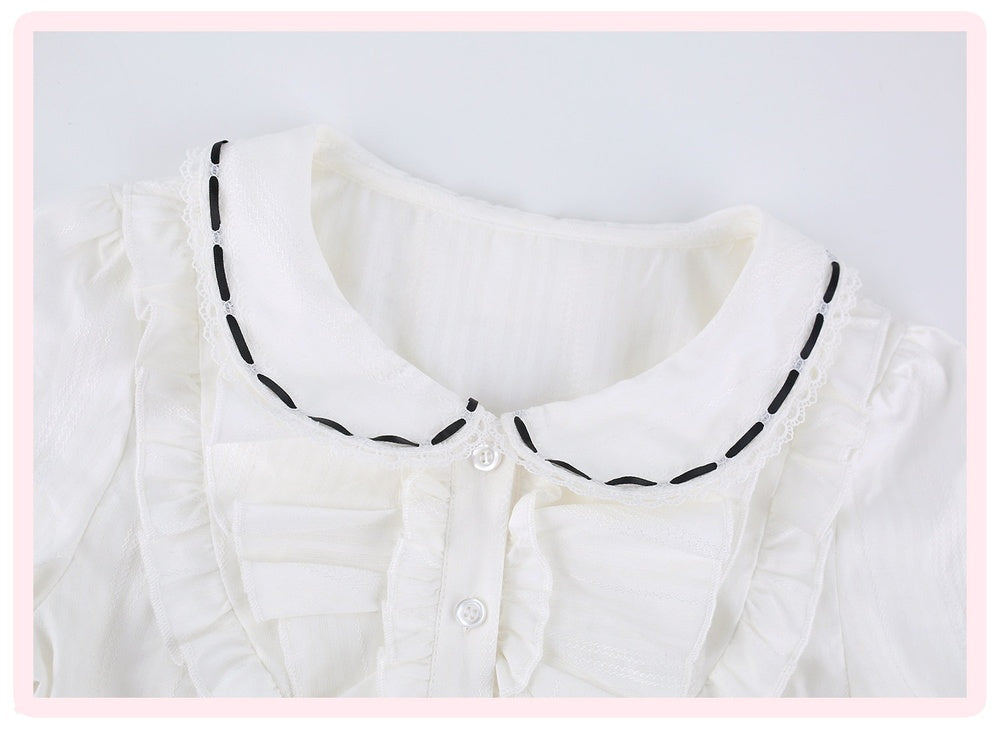 White ruffled blouse with a Peter Pan collar featuring black dashed contrast stitching, shown in a close-up shot.